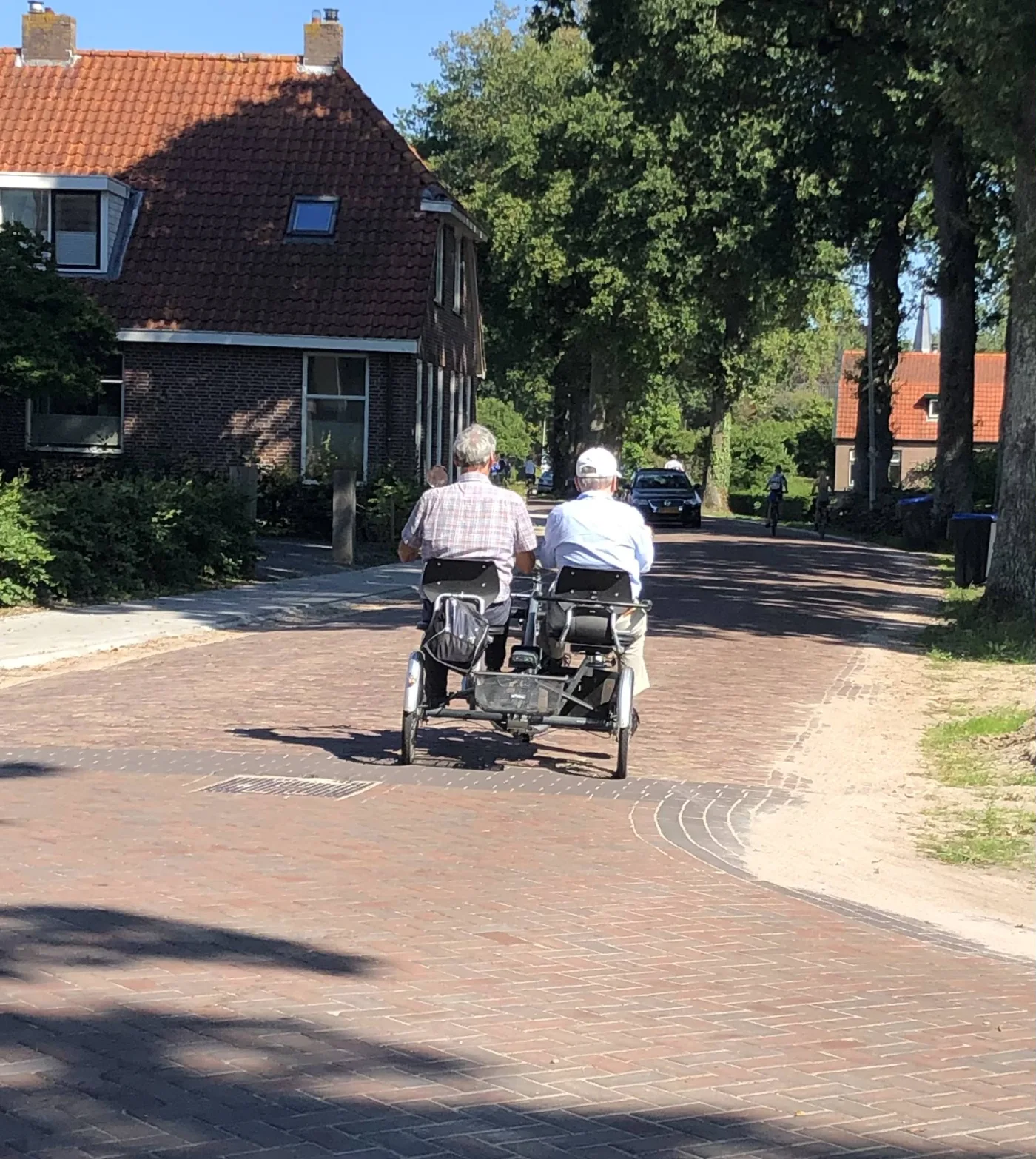 Een bewoner en begeleider samen op de duofiets door een zonnige dorpsstraat